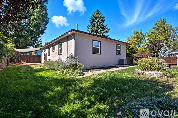 A house with a brown roof and a white fence is surrounded by green grass and trees.