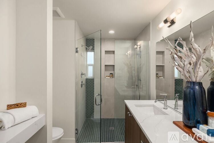 A bathroom with a white counter top and a glass shower stall.