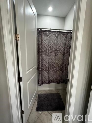 A bathroom with a patterned shower curtain and a black mat on the floor.
