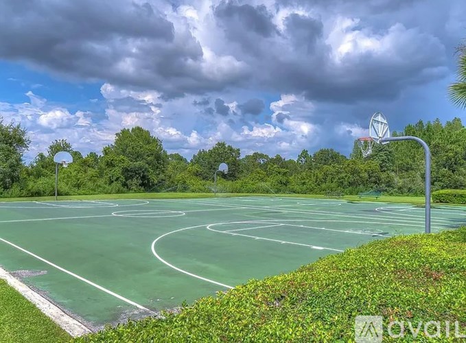 A basketball court surrounded by greenery under a cloudy sky.