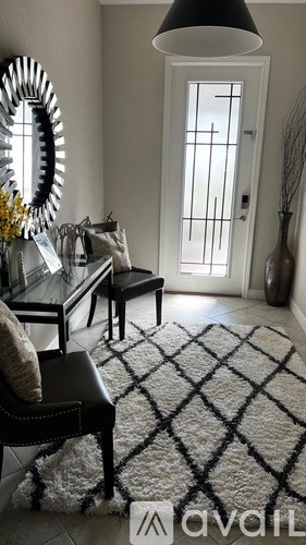 A black and white patterned rug sits in front of a glass table with a black leather chair and a mirror on the wall.