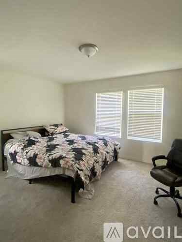 A bedroom with a bed, chair, and window with blinds.
