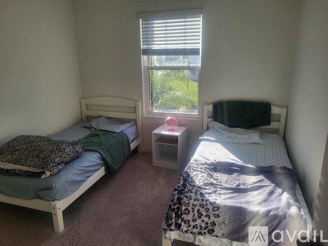 A bedroom with two beds and a window with blinds.