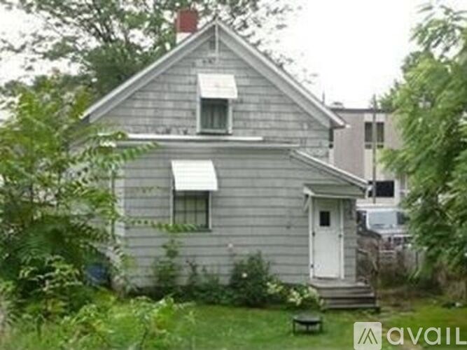 A house with a white door and a window is surrounded by greenery.