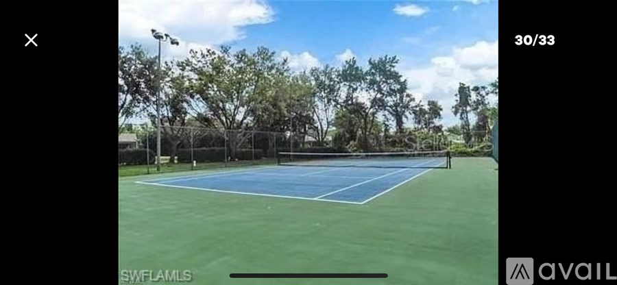 A tennis court surrounded by trees under a blue sky.