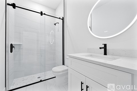 A modern bathroom with a walk-in shower, toilet, and a white sink.