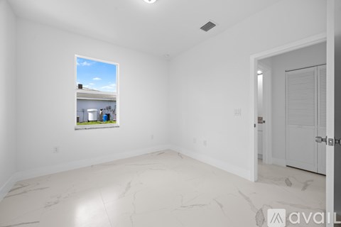A large empty room with a window showing a view of a house and a door on the right.