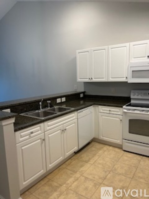 A kitchen with white cabinets and black countertops.