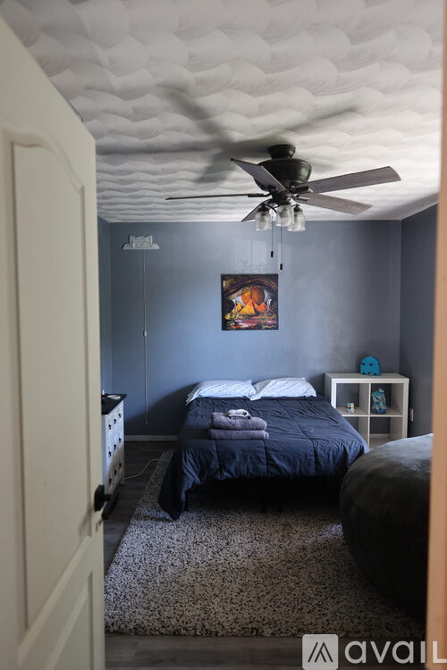 A bedroom with a bed, a ceiling fan, and a painting on the wall.