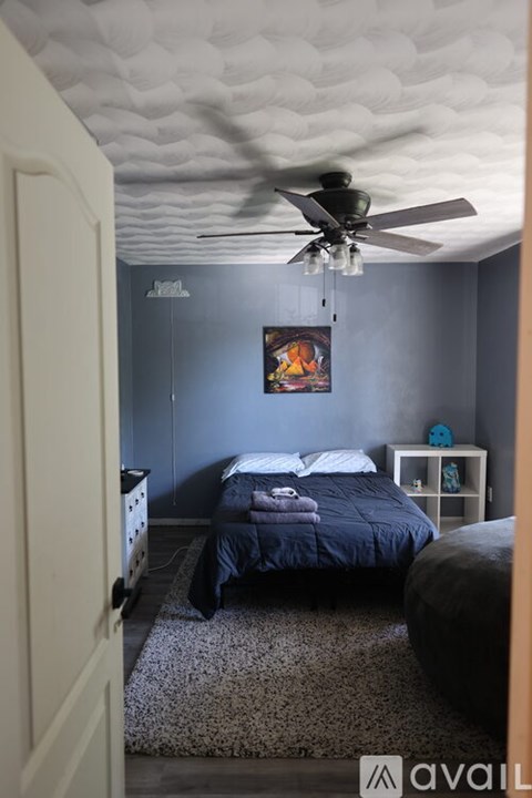 A bedroom with a bed, a ceiling fan, and a painting on the wall.