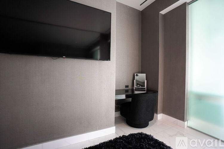A black television is mounted on a wall above a black ottoman.