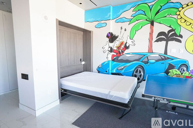 A bedroom with a bed, a table, and a wall mural featuring a cartoon character.