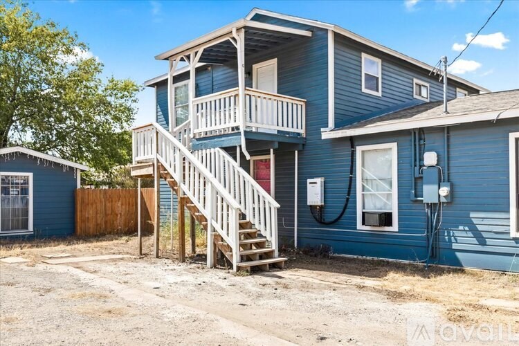 A blue house with a wooden deck and stairs leading to the second floor.