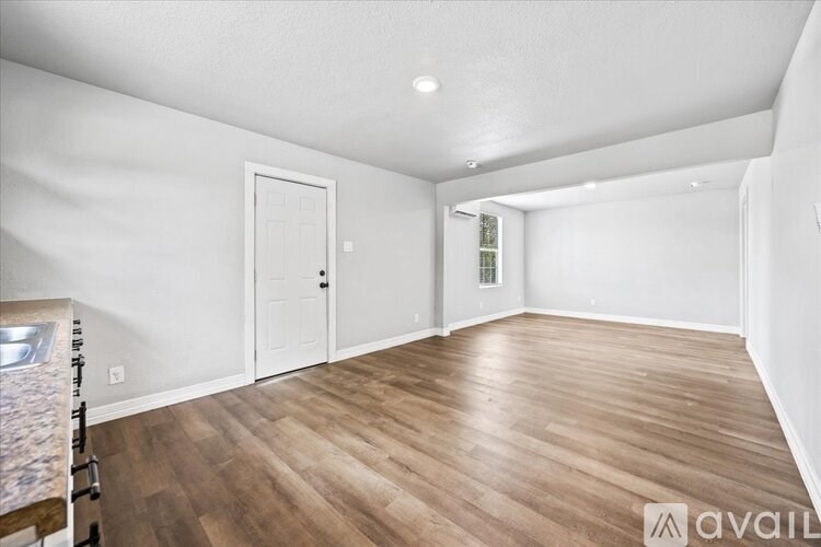 A room with wooden flooring and white walls, with a door and a window.
