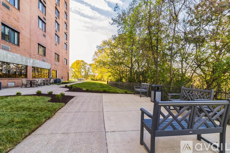 A park with benches and trees in front of a red building.
