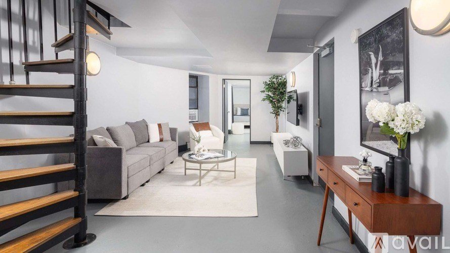 A living room with a grey couch, a glass coffee table, a wooden side table, and a staircase with wooden railings.