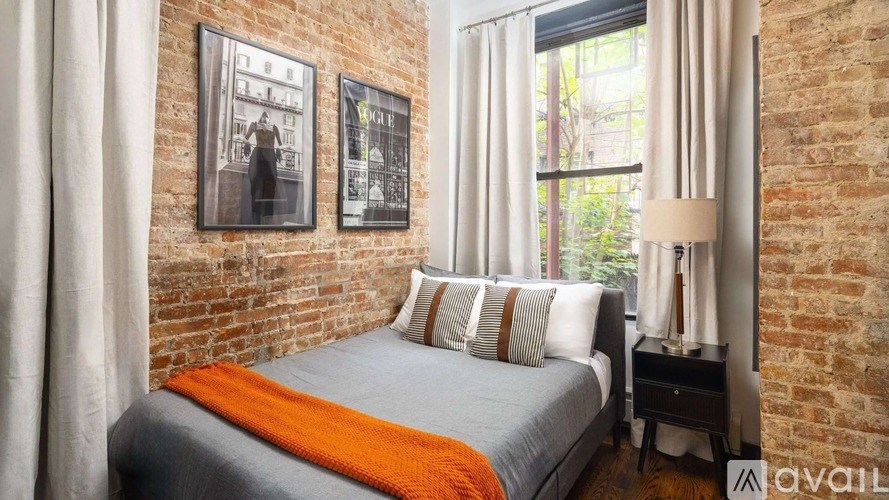 A bedroom with a brick wall and a bed with an orange throw.