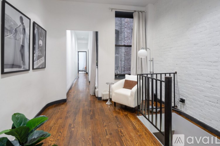 A long hallway with a white chair and a plant on the left and a black railing on the right.