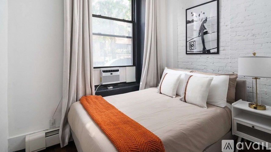 A bedroom with a bed, a window with curtains, and a picture on the wall.