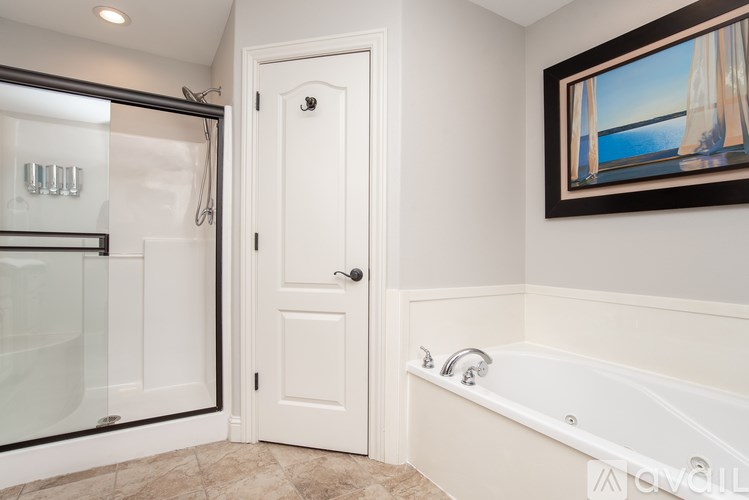 A bathroom with a white door, a bathtub, and a painting on the wall.