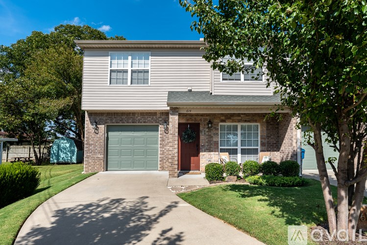 A house with a grey garage door and a red door is surrounded by greenery.