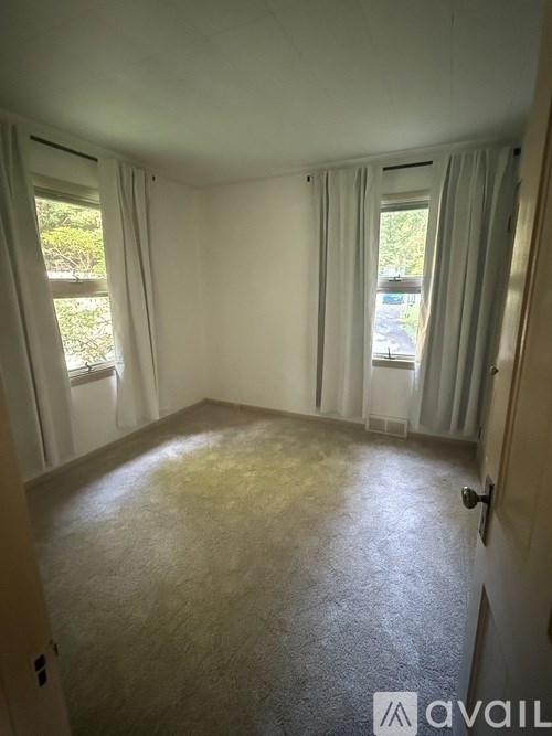 A room with a carpeted floor and two windows with curtains.