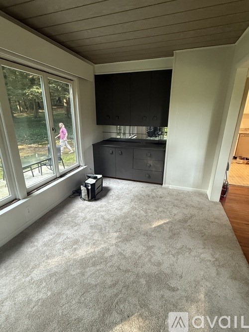 A woman is standing by a window in a room with a grey carpet.