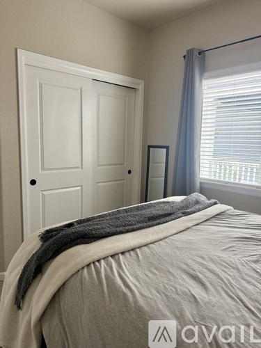 A bedroom with a bed covered in a grey blanket and a white door.