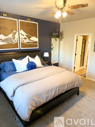 A bedroom with a bed, pillows, a ceiling fan, and a door.