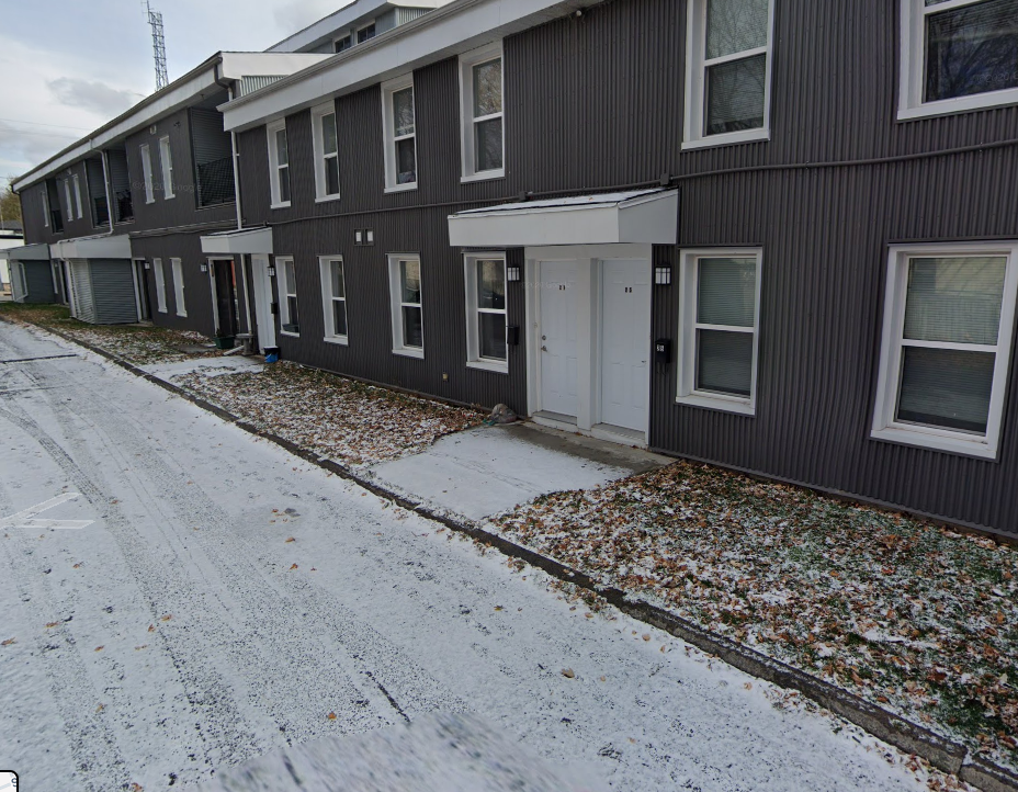 A row of houses with snow on the ground and leaves on the ground.