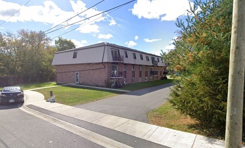 A brick building with a white roof is surrounded by trees and grass.