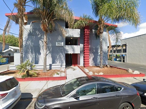 A grey car is parked in front of a building with a red awning.