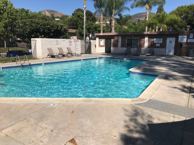 A large outdoor swimming pool surrounded by a concrete patio and a small building.