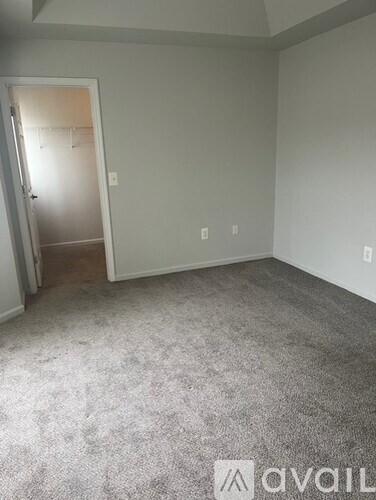 A room with grey carpet and a door leading to another room.
