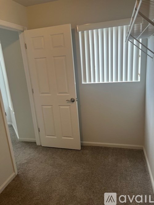 A white door is in a room with carpeted flooring and a window with blinds.