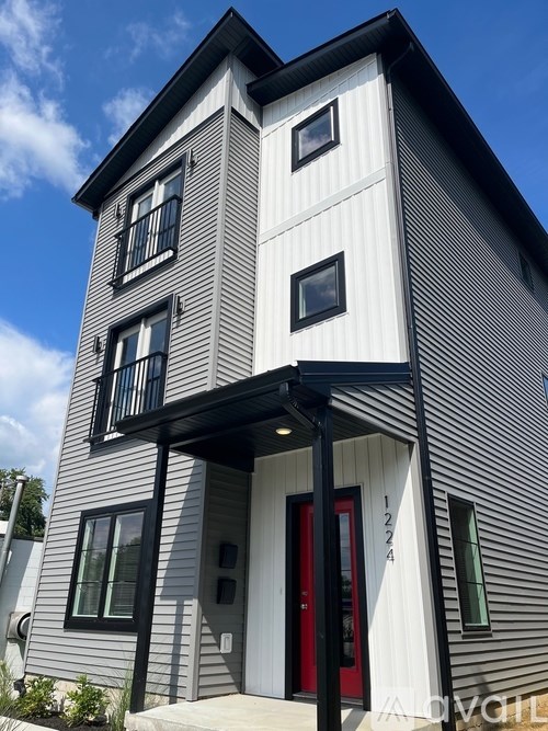 A modern two-story house with a red door and a balcony on the second floor.