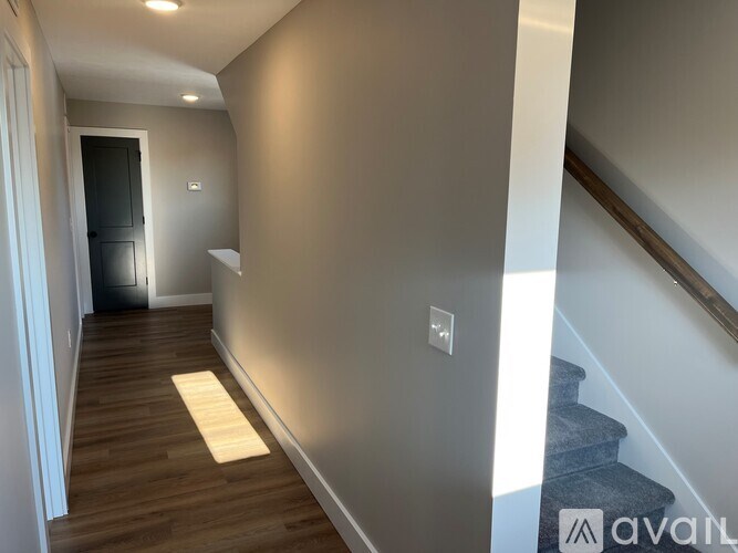 A hallway with wooden floors and a staircase on the right side.