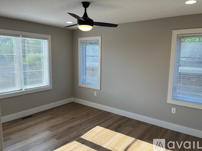 A room with a ceiling fan and two windows.