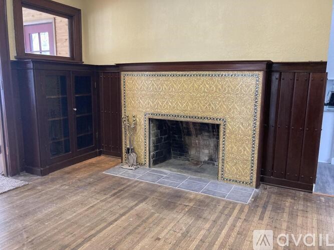 A fireplace with a gold patterned screen is in the middle of a room with wooden floors and a wooden cabinet.