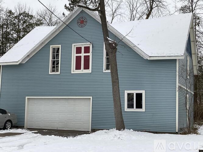 A blue house with a white garage door and a tree in front.