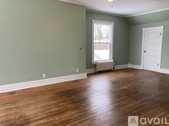 A room with wooden floors and a window with a view of a fence.