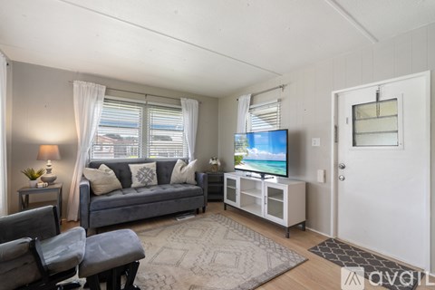 A living room with a grey couch, a chair, a table with a lamp and a plant, a television on a stand, and a rug on the floor.