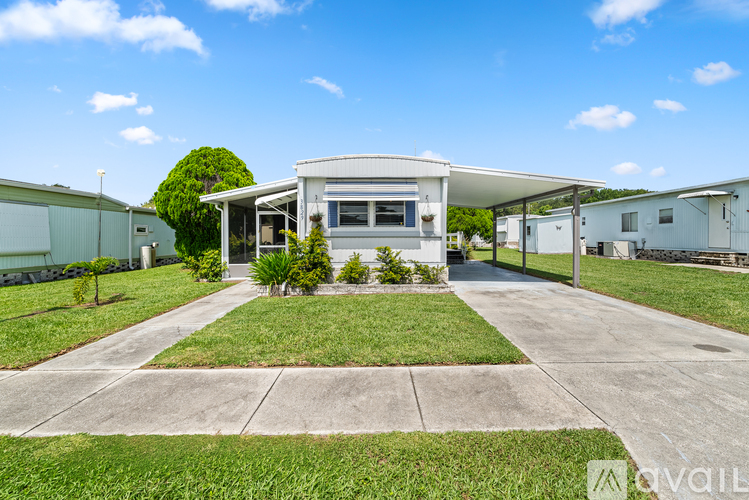 A house with a white exterior and a grey roof is surrounded by a well-maintained lawn and a clear blue sky.