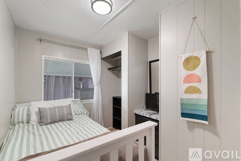 A bedroom with a bed, a desk, and a hanging artwork.