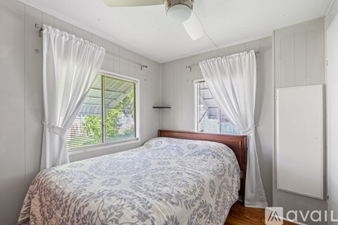 A bedroom with a bed, a window with white curtains, and a ceiling fan.