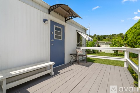 A small white house with a blue door and a wooden deck.