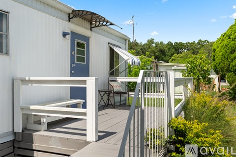 A white house with a blue door and a white bench on the deck.