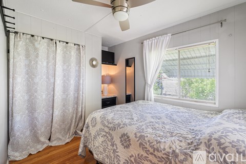 A bedroom with a bed, a window with white curtains, and a ceiling fan.