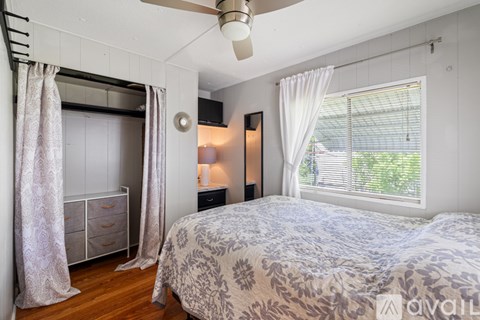 A bedroom with a bed, a ceiling fan, and a window with white curtains.