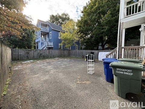 A backyard with a blue house, a fence, and a trash can.